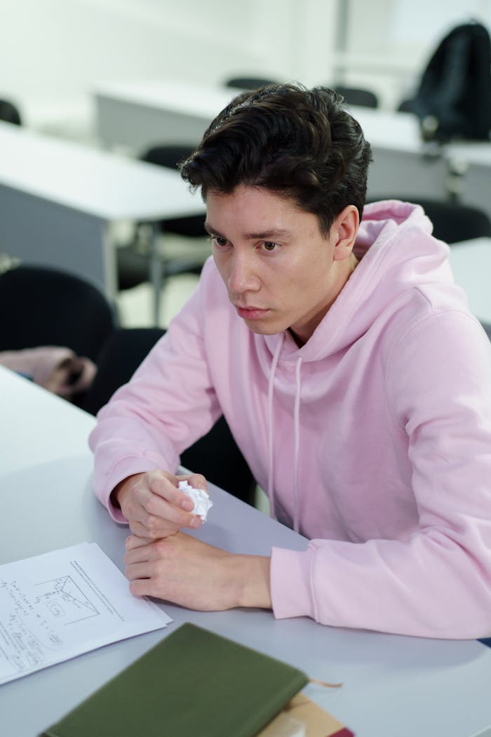 Focused young student wearing a pink hoodie, studying in a classroom setting.